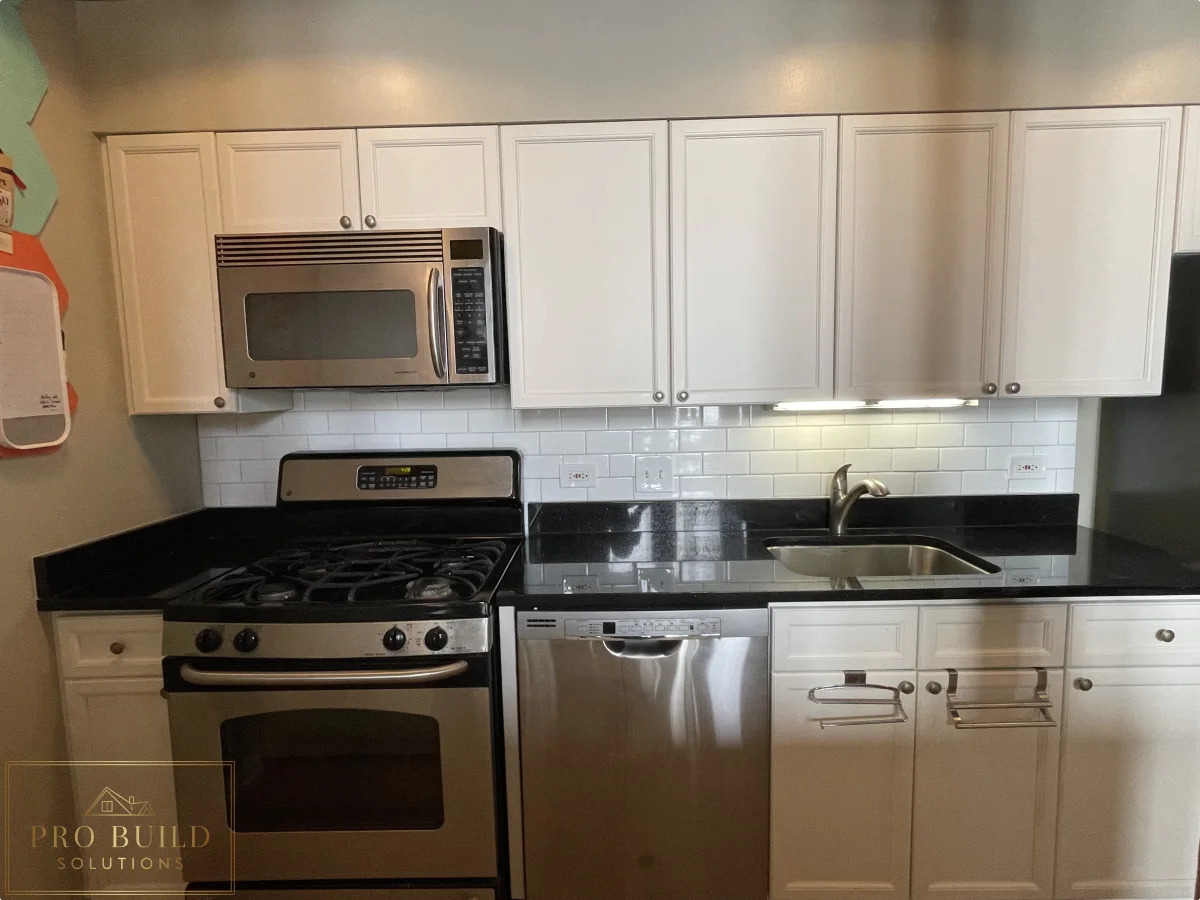 Compact kitchen remodel with stainless steel appliances, white cabinets, black counters, and under-cabinet lighting, Chicago - South Loop, IL