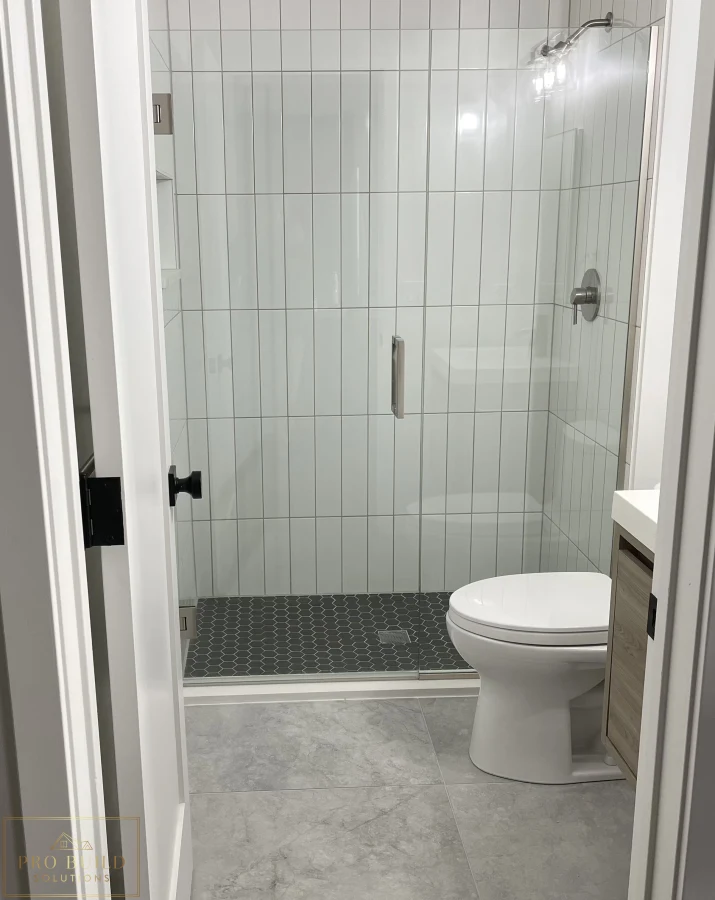 Small bathroom renovation featuring frameless shower door, gray tile flooring, and compact wood-tone vanity, Claredon Hills