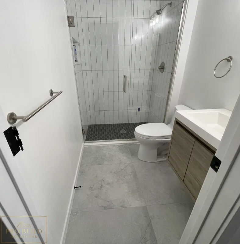 Small bathroom renovation featuring frameless shower door, gray tile flooring, and compact wood-tone vanity, Claredon Hills