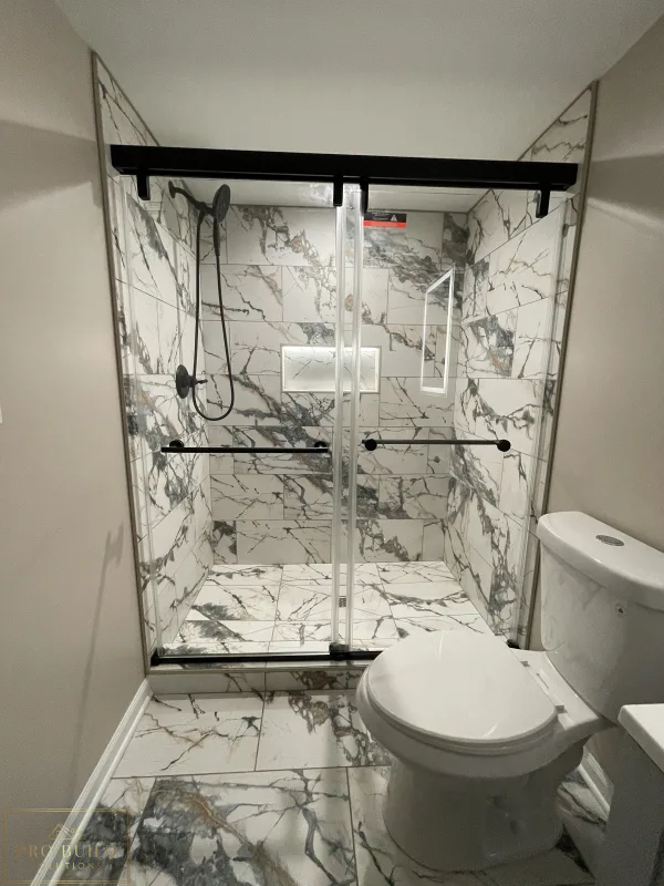Modern bathroom renovation featuring marble-style tile shower, glass enclosure, and black hardware accents, Itasca