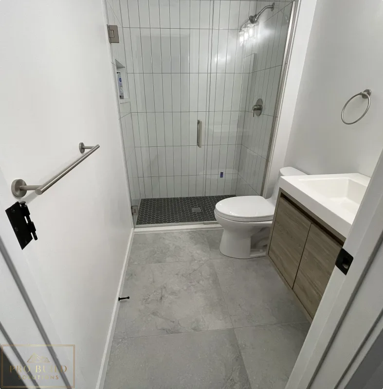 Small bathroom renovation featuring frameless shower door, gray tile flooring, and compact wood-tone vanity, Claredon Hills