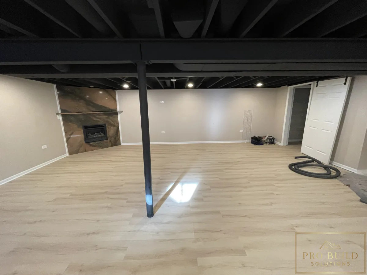 Basement finishing project with modern flooring, painted ceiling beams, and built-in fireplace feature wall, Naperville