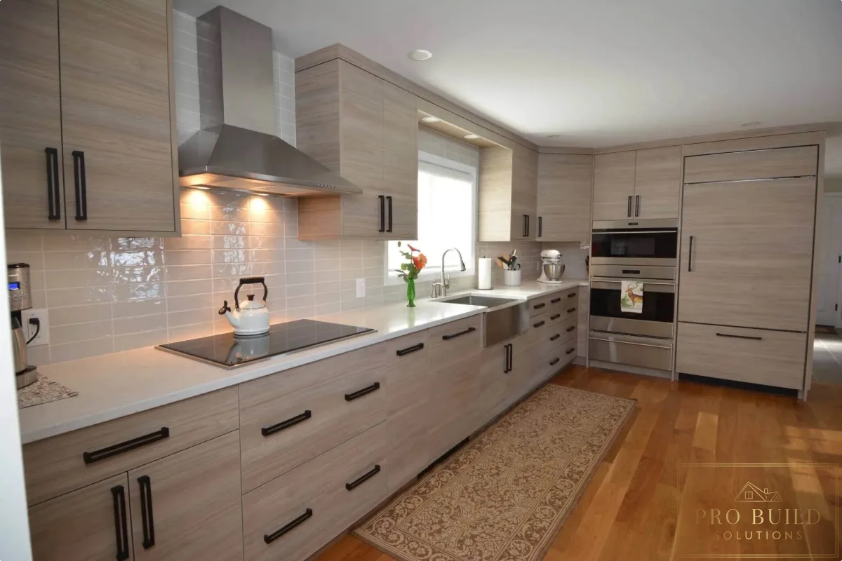 Contemporary galley kitchen featuring natural wood cabinetry, white counters, glossy tile backsplash, and black hardware, Barrington
