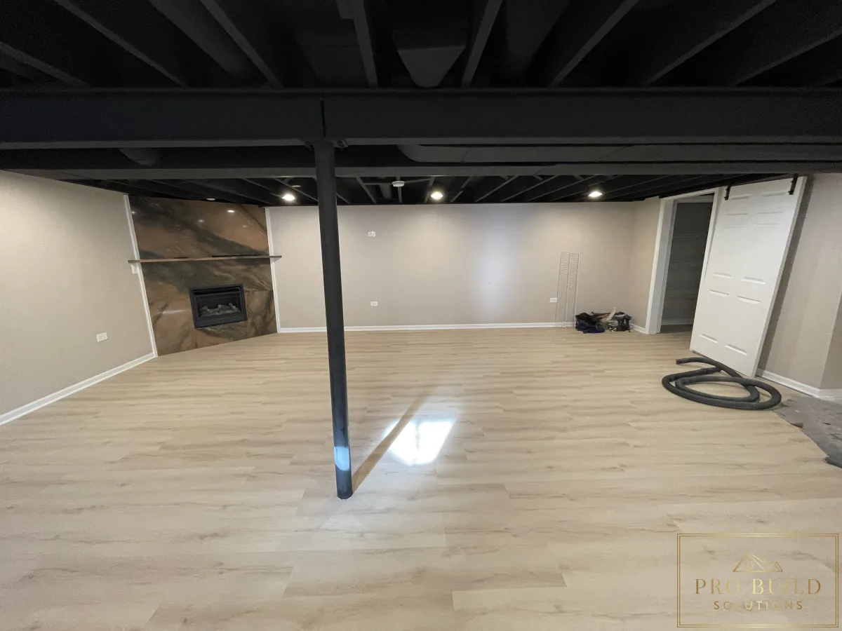 Finished basement remodel with light wood-look flooring, black exposed ceiling, and stone fireplace accent wall, Naperville