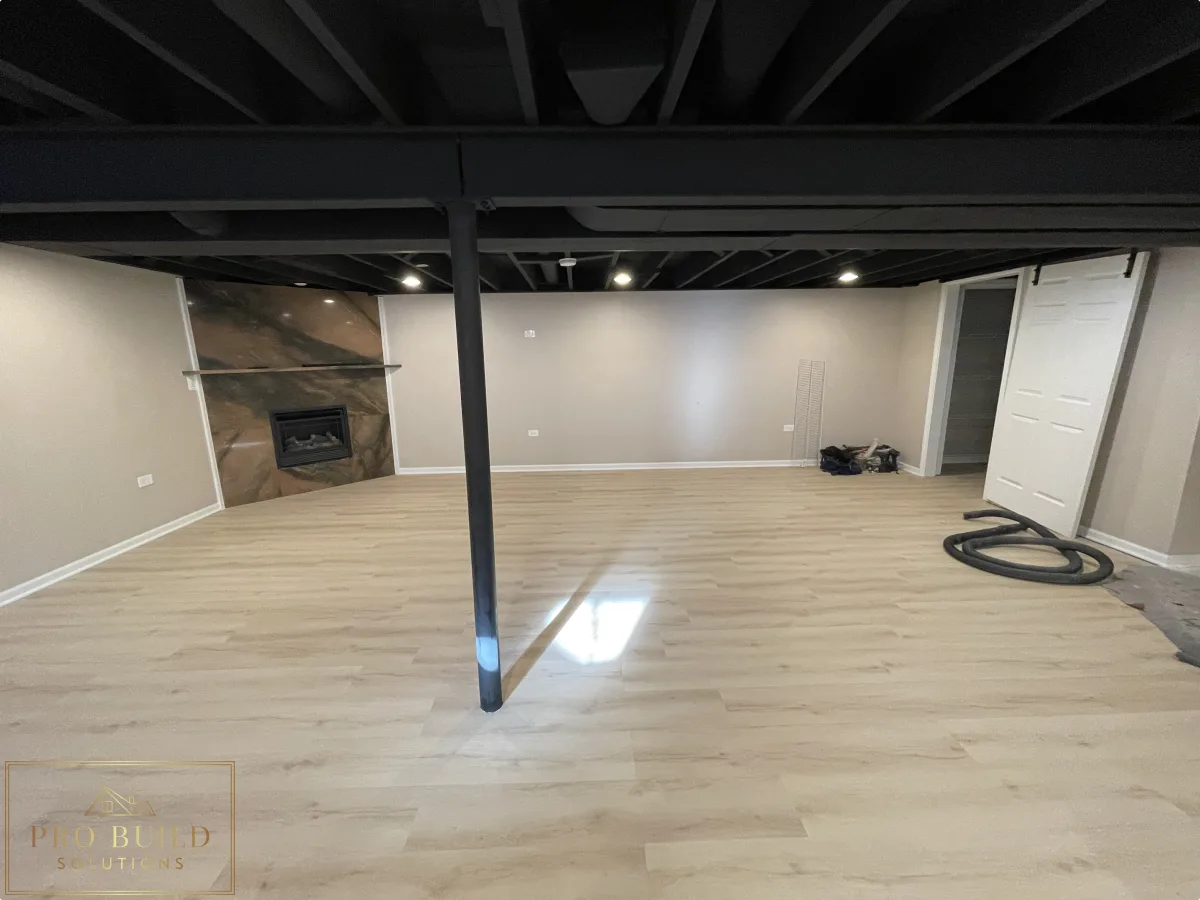 Finished basement remodel with light wood-look flooring, black exposed ceiling, and stone fireplace accent wall, Naperville