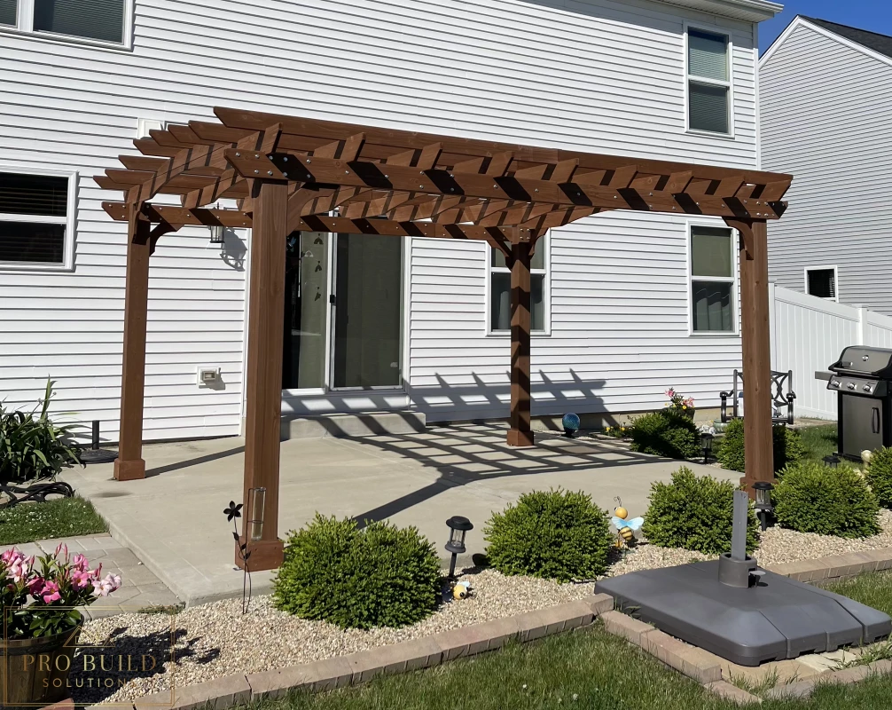 Custom wood pergola over backyard concrete patio with decorative rafters and posts, Joliet, IL