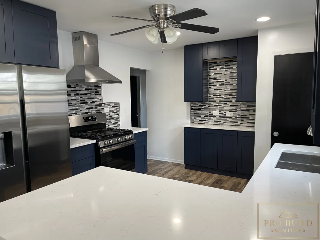 Modern kitchen remodel featuring dark blue cabinets, white countertops, stainless range hood, and tile backsplash, Lemont