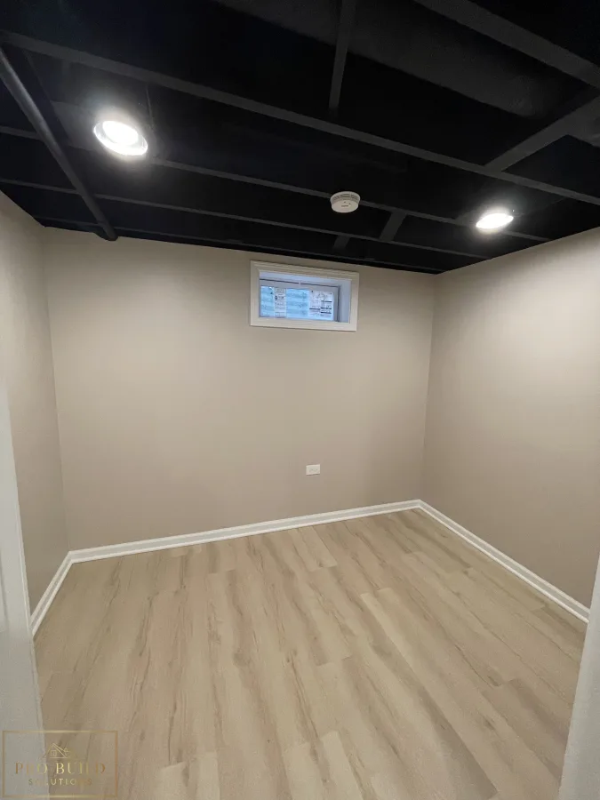 Basement remodel featuring neutral walls, modern plank flooring, painted ceiling beams, and updated lighting, Bartlett