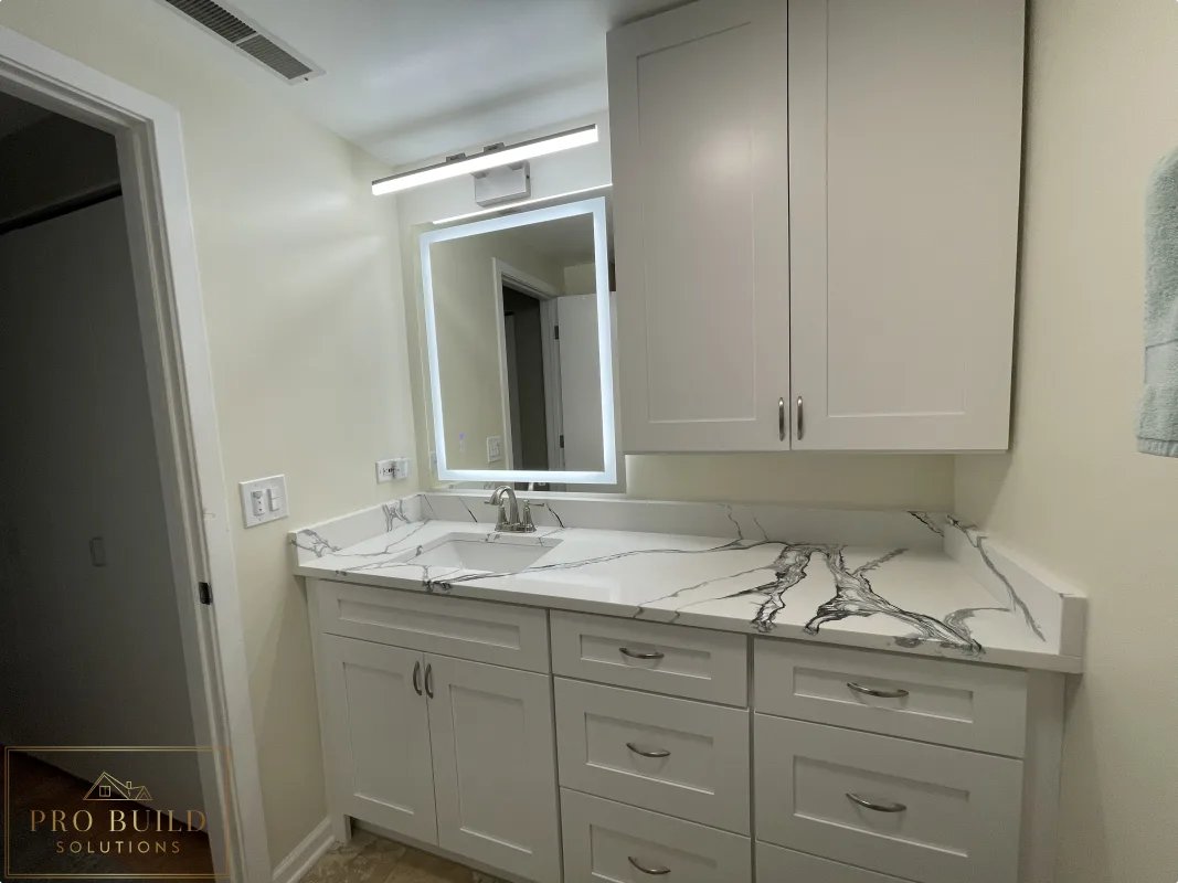 Side View of bathroom vanity remodel with shaker cabinetry, stone-look countertop, wall storage, modern illuminated mirror and new led exhaust fan., Lisle