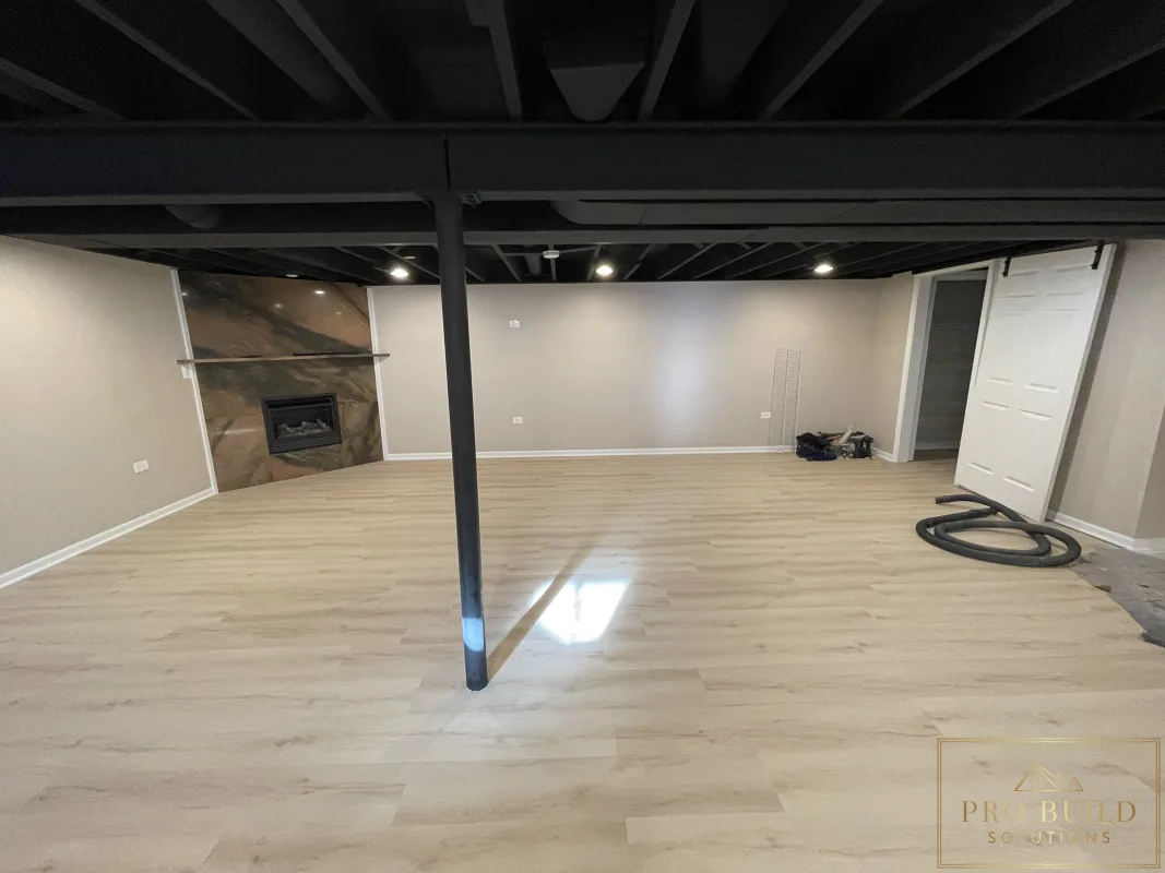 Finished basement living room with exposed black ceiling, neutral walls, and large open recreation space, Naperville