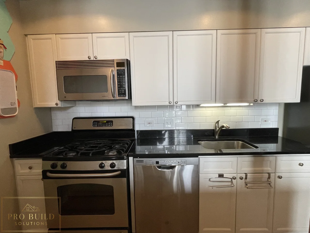 Compact kitchen remodel with stainless steel appliances, white cabinets, black counters, and under-cabinet lighting, Chicago - South Loop, IL