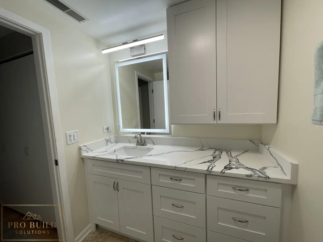 Side View of bathroom vanity remodel with shaker cabinetry, stone-look countertop, wall storage, modern illuminated mirror and new led exhaust fan., Lisle