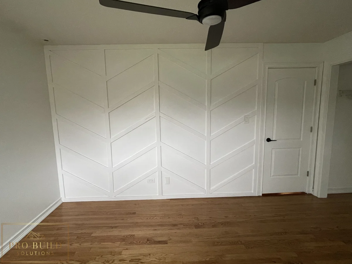 Decorative wall molding installation with chevron-style design, white paint, and warm wood flooring, Wheaton, IL